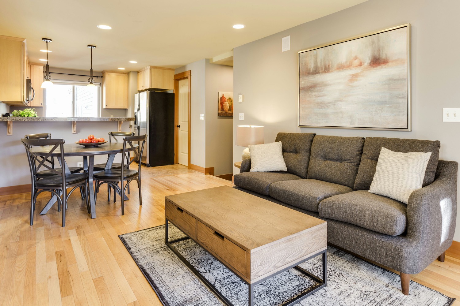 A light-filled living room with a sofa, wood coffee table and open kitchen